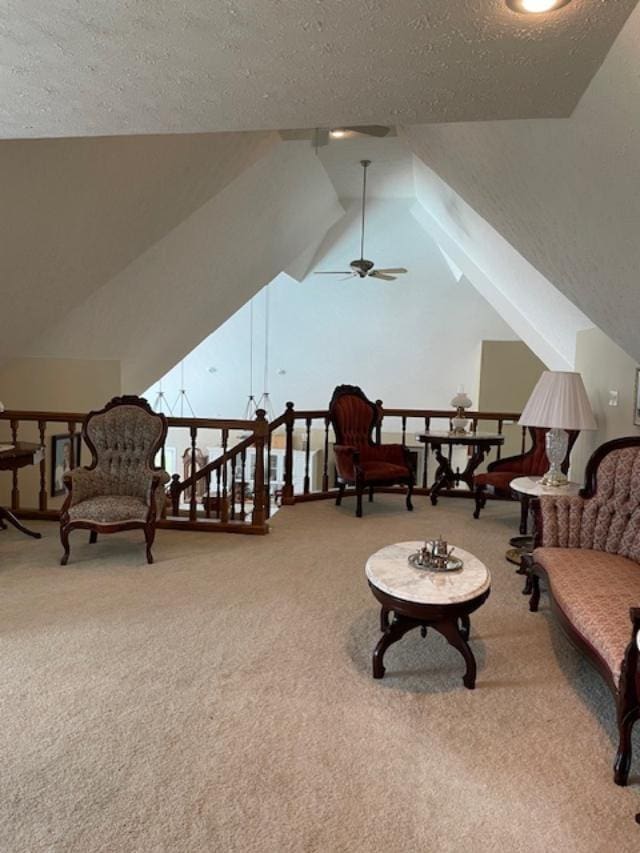 living area featuring ceiling fan, lofted ceiling, carpet flooring, and a textured ceiling