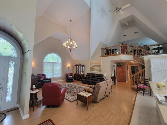 living room with ceiling fan with notable chandelier, high vaulted ceiling, and light wood-type flooring