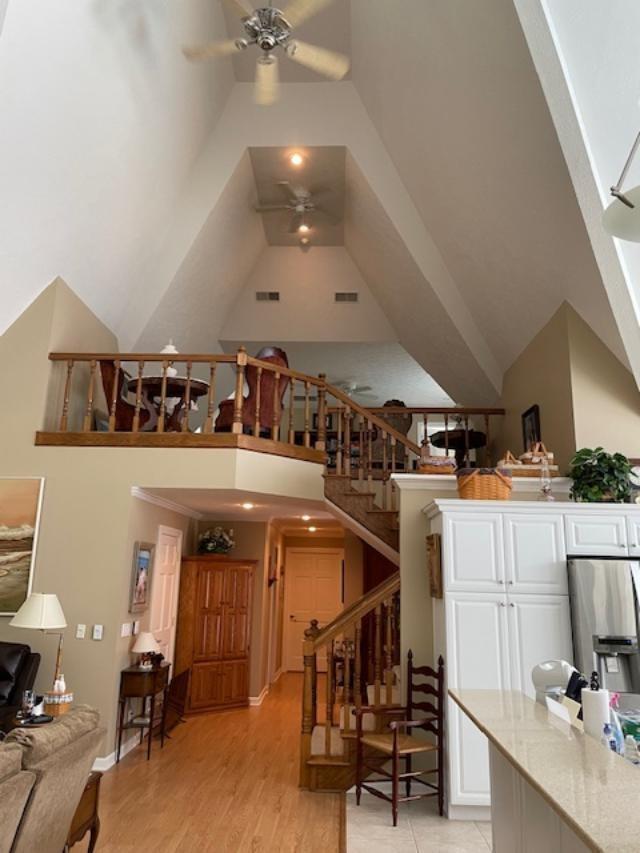 bar with stainless steel refrigerator with ice dispenser, high vaulted ceiling, light wood-type flooring, light stone countertops, and white cabinets