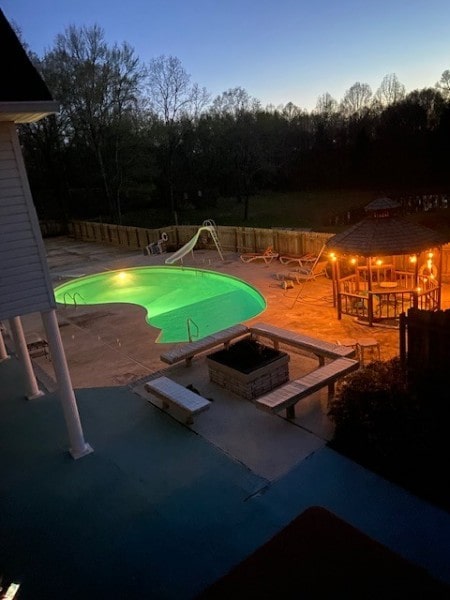 pool at dusk featuring an outdoor fire pit, a water slide, a diving board, and a patio area