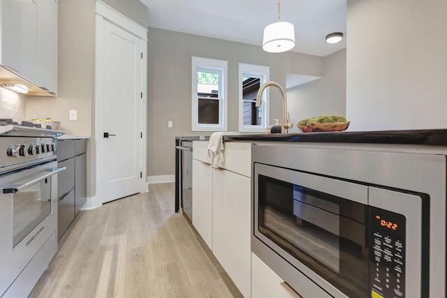 kitchen featuring modern cabinets, appliances with stainless steel finishes, decorative light fixtures, light wood-style floors, and white cabinetry