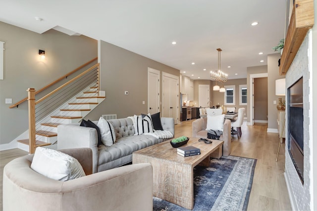 living room with recessed lighting, light wood-style floors, stairs, a glass covered fireplace, and an inviting chandelier