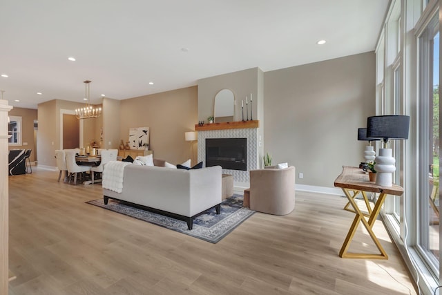 living area featuring recessed lighting, light wood-style flooring, a glass covered fireplace, a chandelier, and baseboards