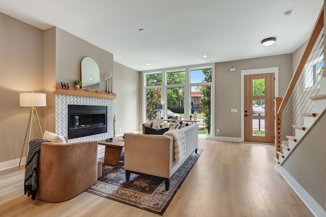 living room featuring stairway, a tile fireplace, light wood-style flooring, and baseboards