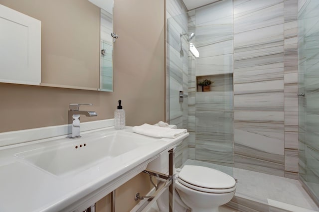 bathroom with sink, a tile shower, and toilet