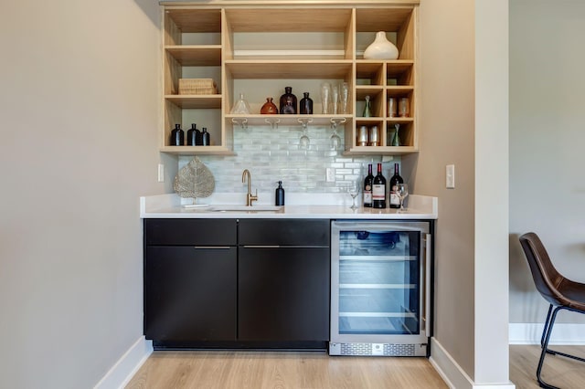 bar featuring light wood finished floors, beverage cooler, tasteful backsplash, indoor wet bar, and a sink