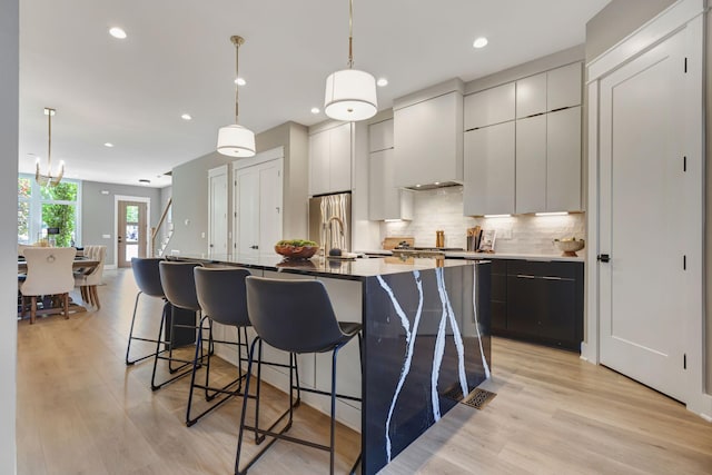 kitchen featuring custom exhaust hood, an island with sink, light hardwood / wood-style flooring, and decorative light fixtures