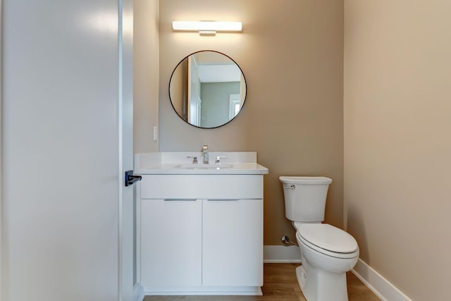 half bath featuring wood finished floors, vanity, toilet, and baseboards