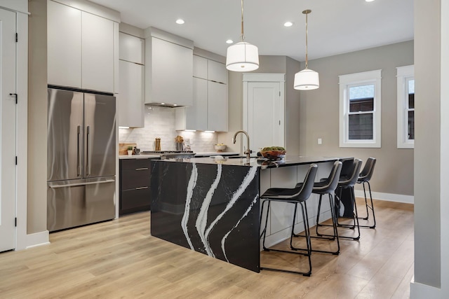 kitchen featuring high end refrigerator, a kitchen breakfast bar, decorative backsplash, light wood finished floors, and custom range hood