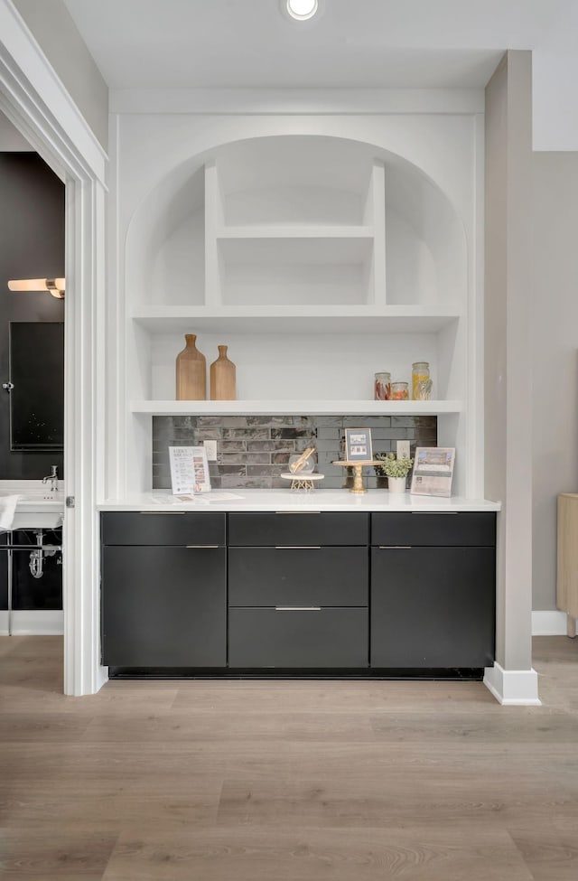 bar with light wood-style floors, baseboards, built in features, and a sink