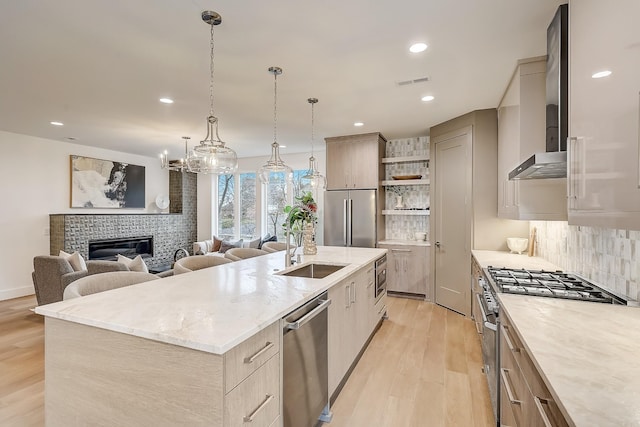 kitchen featuring pendant lighting, sink, stainless steel appliances, a fireplace, and a center island with sink