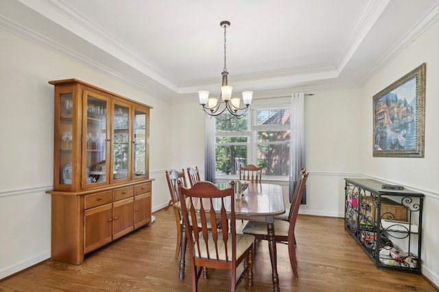 dining space with crown molding, light hardwood / wood-style floors, a chandelier, and a raised ceiling