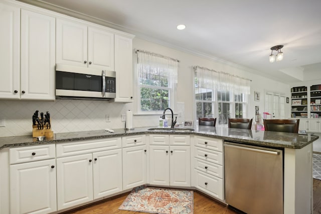 kitchen featuring white cabinetry, stainless steel appliances, dark stone countertops, sink, and kitchen peninsula