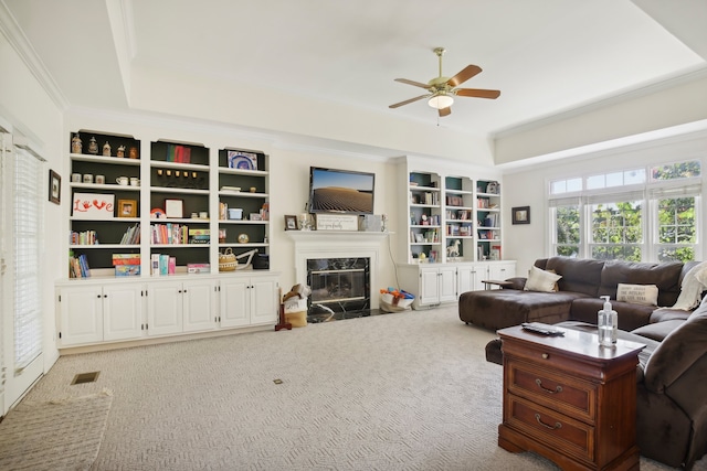 carpeted living room with a fireplace, a tray ceiling, ceiling fan, and ornamental molding