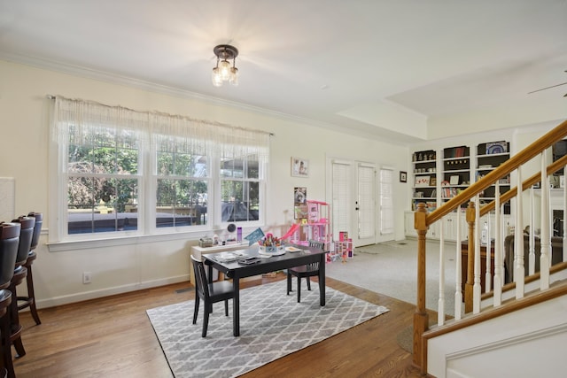 dining room with built in shelves, a raised ceiling, ornamental molding, and wood-type flooring