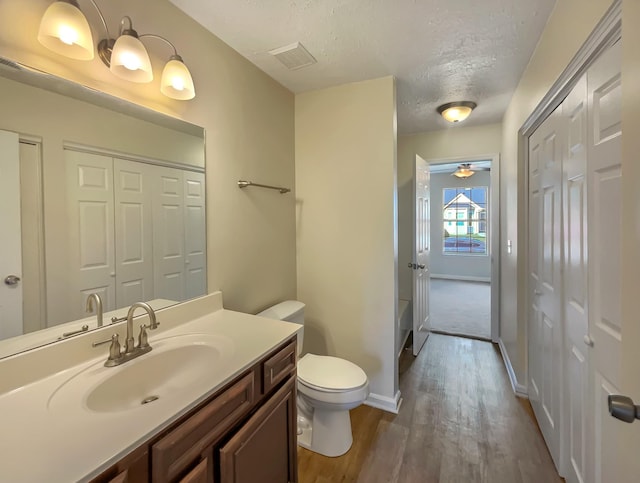 bathroom with ceiling fan, a textured ceiling, toilet, vanity, and hardwood / wood-style flooring