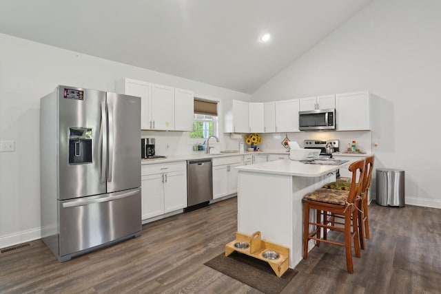 kitchen with appliances with stainless steel finishes, a breakfast bar, high vaulted ceiling, white cabinets, and a center island