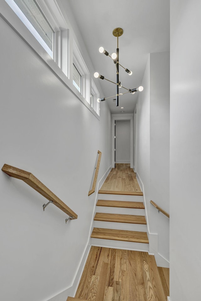 staircase with hardwood / wood-style floors and a chandelier