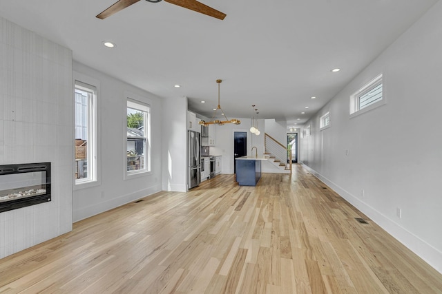 unfurnished living room with a tiled fireplace, sink, ceiling fan, and light hardwood / wood-style flooring