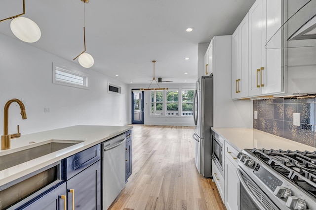 kitchen featuring sink, hanging light fixtures, appliances with stainless steel finishes, decorative backsplash, and white cabinets