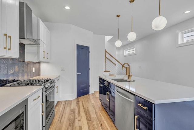 kitchen with blue cabinetry, wall chimney exhaust hood, white cabinetry, hanging light fixtures, and appliances with stainless steel finishes