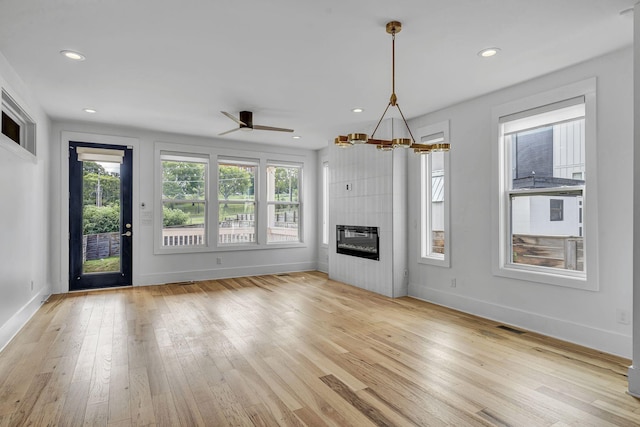 unfurnished living room with an inviting chandelier, a fireplace, light hardwood / wood-style flooring, and a healthy amount of sunlight