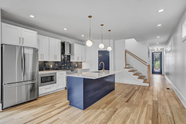 kitchen featuring white cabinets, appliances with stainless steel finishes, a kitchen island with sink, and wall chimney range hood