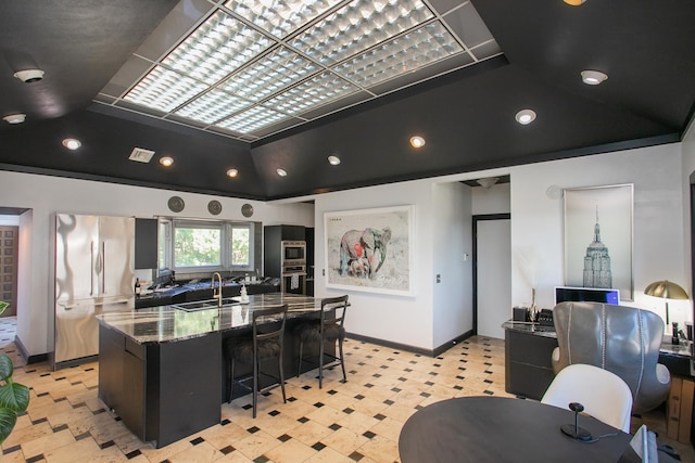 kitchen with a spacious island, lofted ceiling, sink, dark stone countertops, and stainless steel refrigerator