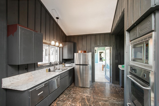 kitchen with vaulted ceiling, stainless steel appliances, wooden walls, and sink