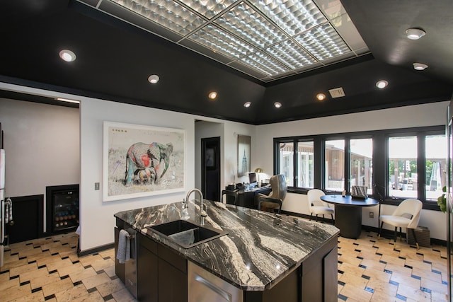 kitchen with lofted ceiling, sink, a center island with sink, dark stone counters, and beverage cooler