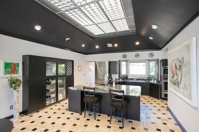 kitchen with sink, stainless steel fridge, a kitchen breakfast bar, stone countertops, and vaulted ceiling