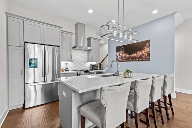 kitchen with wall chimney range hood, a center island with sink, sink, and appliances with stainless steel finishes