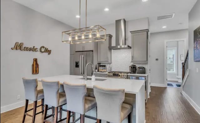 kitchen with wall chimney range hood, sink, gray cabinetry, stainless steel appliances, and a kitchen breakfast bar