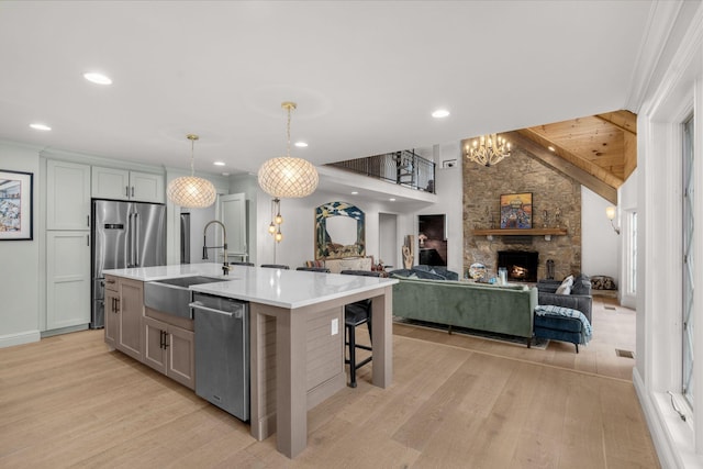 kitchen featuring sink, stainless steel appliances, a stone fireplace, pendant lighting, and a kitchen island with sink