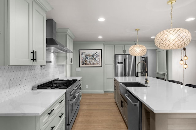 kitchen with appliances with stainless steel finishes, tasteful backsplash, wall chimney exhaust hood, a kitchen island with sink, and decorative light fixtures