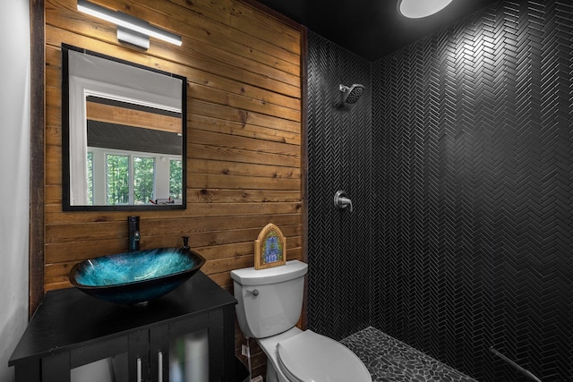 bathroom with a tile shower, wooden walls, vanity, and toilet