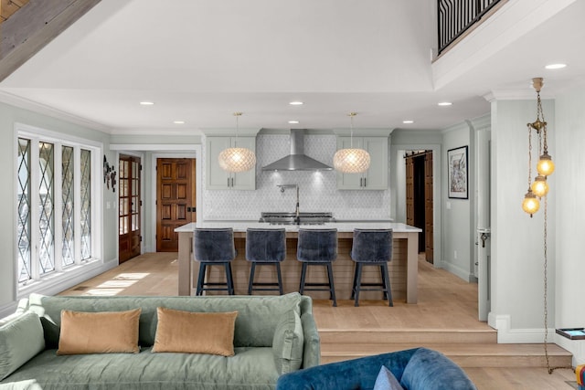 kitchen featuring a kitchen bar, decorative backsplash, a kitchen island with sink, wall chimney range hood, and decorative light fixtures