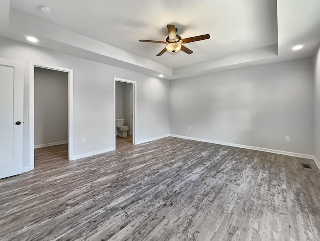 unfurnished bedroom with ensuite bath, ceiling fan, a tray ceiling, and hardwood / wood-style floors