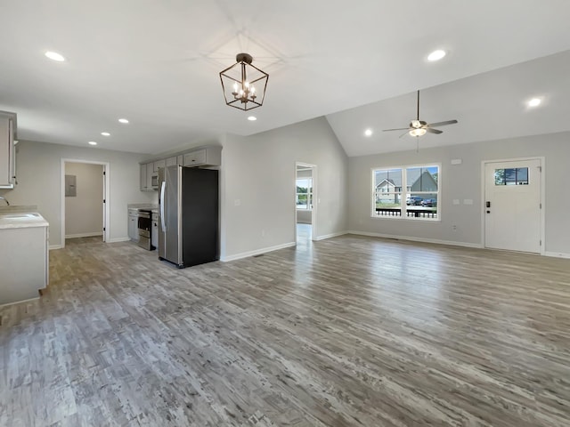 unfurnished living room featuring sink, electric panel, lofted ceiling, light wood-type flooring, and ceiling fan with notable chandelier