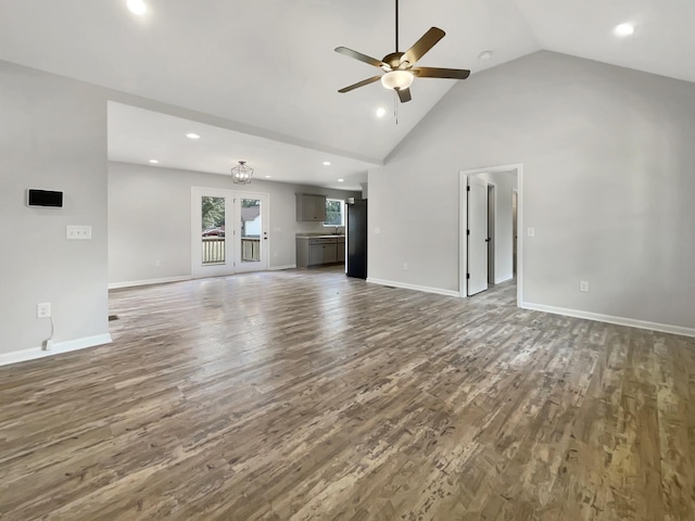 unfurnished living room with ceiling fan with notable chandelier, high vaulted ceiling, dark hardwood / wood-style flooring, and french doors