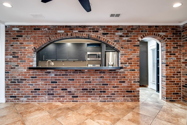 interior space featuring crown molding, stainless steel appliances, ceiling fan, and brick wall