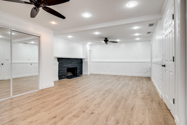 unfurnished living room featuring ceiling fan, ornamental molding, a stone fireplace, and light wood-type flooring