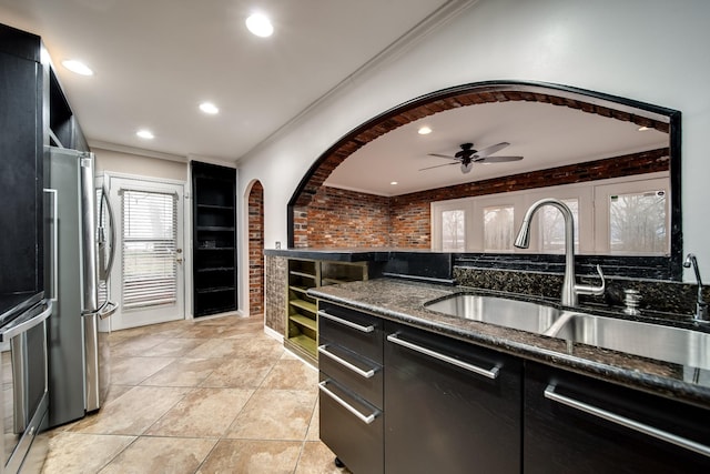 kitchen with brick wall, appliances with stainless steel finishes, sink, dark stone countertops, and light tile patterned floors