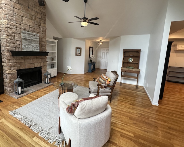 living room featuring a stone fireplace, high vaulted ceiling, ceiling fan, and light wood-type flooring