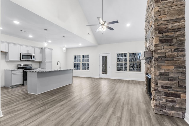 kitchen with hanging light fixtures, stainless steel appliances, light stone counters, an island with sink, and a stone fireplace