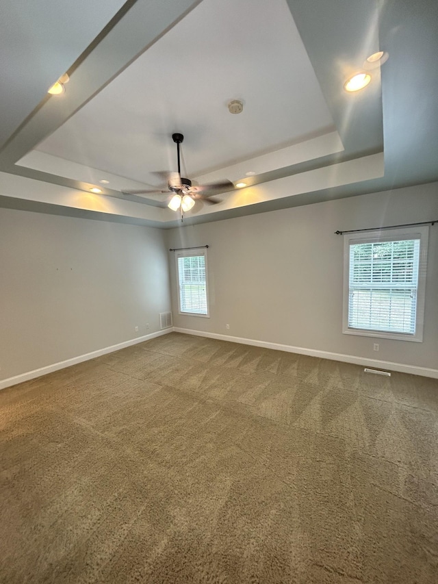 empty room featuring a tray ceiling, dark carpet, visible vents, and baseboards