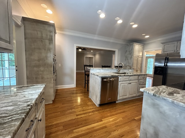 kitchen with appliances with stainless steel finishes, hardwood / wood-style floors, sink, crown molding, and light stone countertops