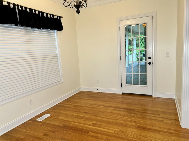 unfurnished room featuring wood-type flooring, crown molding, and an inviting chandelier