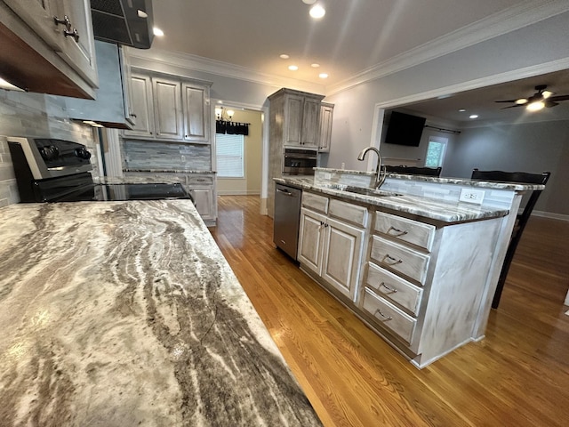kitchen featuring light stone counters, a sink, appliances with stainless steel finishes, light wood-type flooring, and backsplash