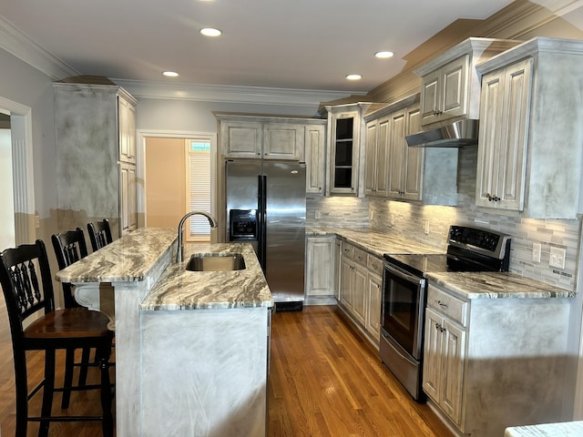 kitchen featuring a breakfast bar area, under cabinet range hood, a sink, appliances with stainless steel finishes, and light stone countertops
